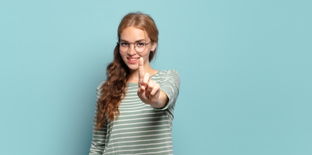 Mulher loira bonita sorrindo com orgulho e confiança fazendo a pose número um triunfantemente, sentindo-se uma líder