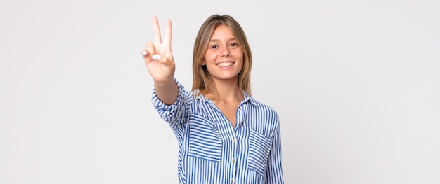 Mulher loira bonita sorrindo e parecendo amigável, mostrando o número três ou o terceiro com a mão para a frente, em contagem regressiva