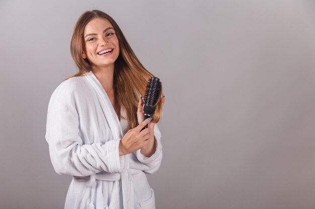 Mulher loira brasileira mostrando cabelo maravilhoso vestido com um roupão usando escova de cabelo