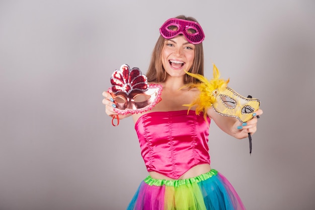 Mulher loira brasileira vestida com roupas de carnaval rosa segurando máscaras de carnaval