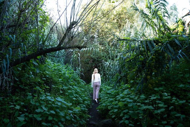 Mulher loira caminhando cercada de plantas no meio da natureza