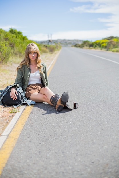 Mulher loira cansada sentada na beira da estrada