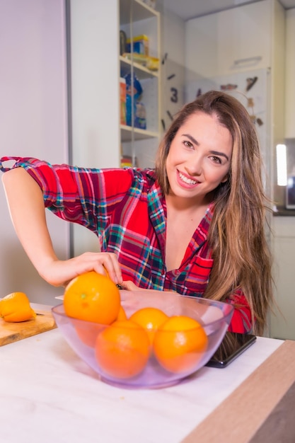 Mulher loira caucasiana tomando um suco de laranja fresco no café da manhã na cozinha