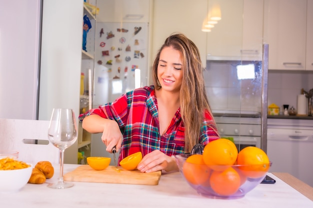 Mulher loira caucasiana tomando um suco de laranja fresco no café da manhã na cozinha