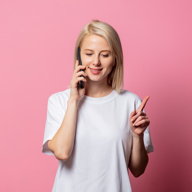 Mulher loira com camiseta branca e celular rosa