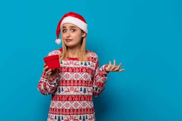 Mulher loira com chapéu de Papai Noel se sentindo perplexa e confusa, duvidando, ponderando ou escolhendo diferentes opções com expressão engraçada