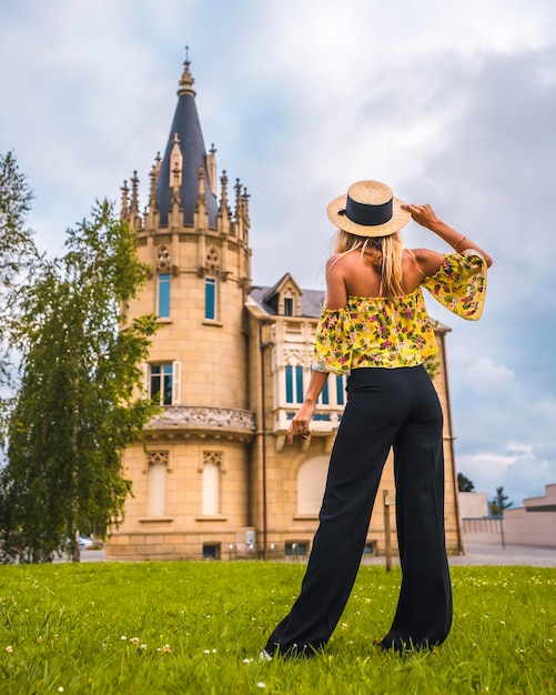 Mulher loira com uma roupa vintage amarela com um chapéu andando ao lado de um castelo na parte de trás