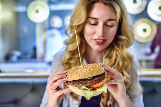 Mulher loira comendo um hamburguer grande e clássico em um restaurante