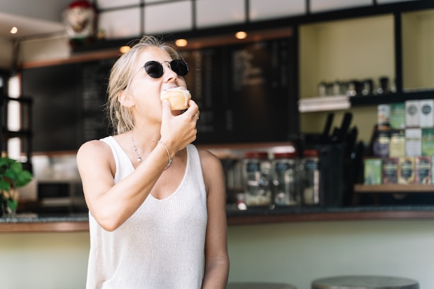 Mulher loira comendo um rolo de canela em um café