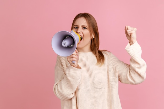 Mulher loira concentrada protestando com o braço levantado e gritando no megafone olhando para a câmera