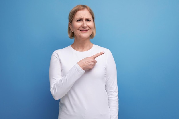 Mulher loira de 50 anos com uma camisola branca relata as notícias em um fundo de estúdio com espaço de cópia