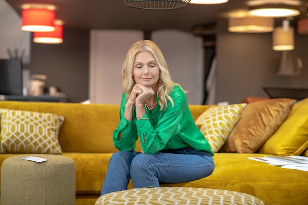 Mulher loira de blusa verde, sentado em um sofá amarelo