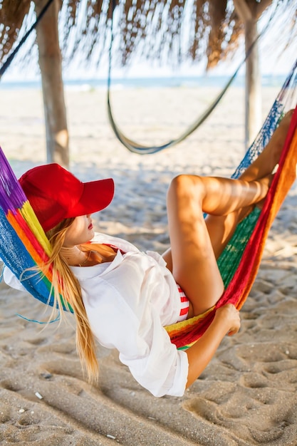 Mulher loira de boné vermelho relaxando em uma rede na praia