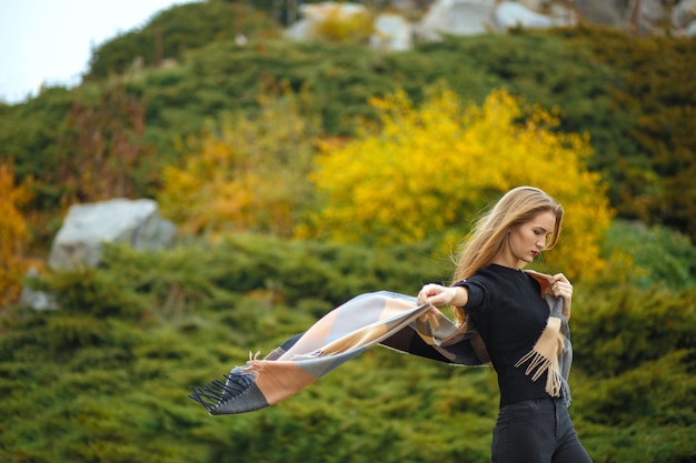 Mulher loira de cabelos compridos elegante usando lenço esvoaçante, posando no jardim botânico. Espaço para texto