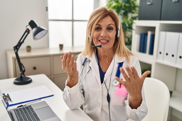 Mulher loira de meia-idade vestindo uniforme médico tendo teleconsulta médica na clínica