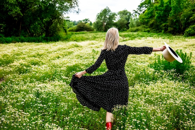 Mulher loira de vestido preto no campo camomiles flores campo