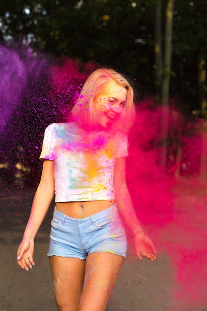 Mulher loira descolada em camiseta branca e shorts jeans posando com pó de Holi vermelho