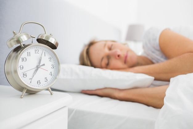 Mulher loira dormindo na cama enquanto seu alarme mostra o início do tempo
