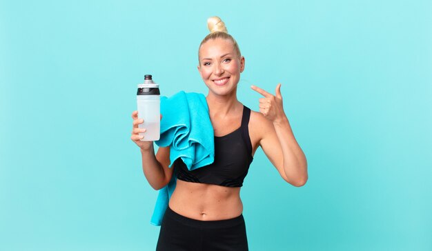 Mulher loira e bonita sorrindo com confiança, apontando para o próprio sorriso largo. conceito de fitness