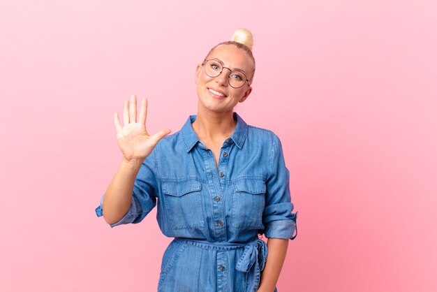 Mulher loira e bonita sorrindo e parecendo amigável, mostrando o número cinco