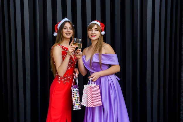 Mulher loira e morena em elegantes vestidos de noite posando com taças de champanhe