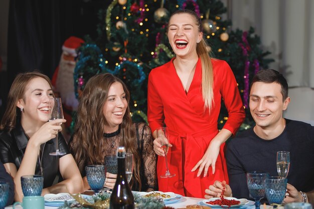 Mulher loira em vermelhos brindes aos amigos à mesa no Natal e no ano novo.