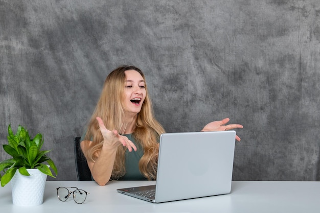 Mulher loira em vestido elegante posando com laptop e flor verde