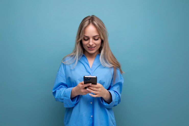 Mulher loira encantadora conversando em um smartphone em um fundo azul brilhante