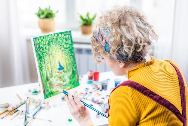 Mulher loira encaracolada pintando um quadro pela janela