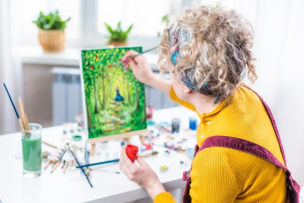 Mulher loira encaracolada pintando um quadro pela janela