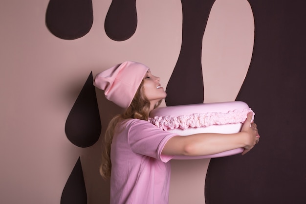 Mulher loira engraçada em t-shirt rosa e boné se divertindo com o macaroon de bolo grande. Conceito de férias