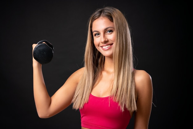 Mulher loira esporte jovem fazendo Halterofilismo sobre parede preta isolada