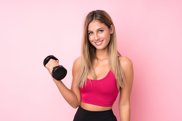 Mulher loira esporte jovem isolado rosa fazendo levantamento de peso com kettlebell