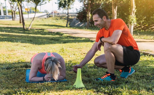 Mulher loira fazendo pranchas em um parque com um personal trainer ao lado