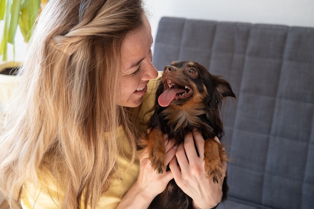 Mulher loira feliz com engraçado terrier de brinquedo russo marrom. olhem uns para os outros. Conceito de cuidados de animais de estimação. amor e amizade.