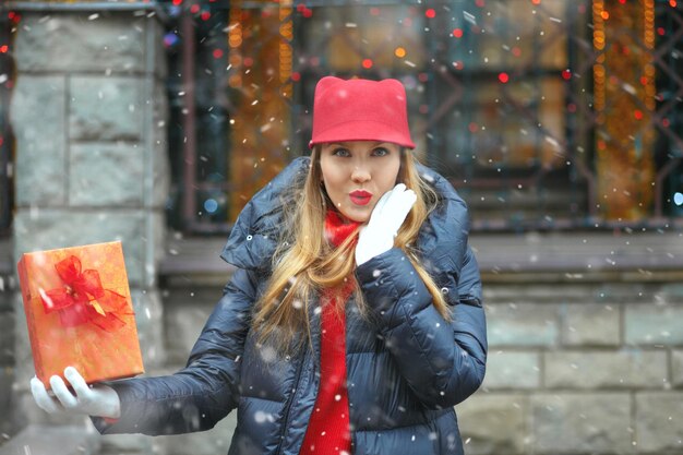 Mulher loira feliz com uma caixa de presente no mercado de rua de Natal durante a queda de neve. Espaço vazio