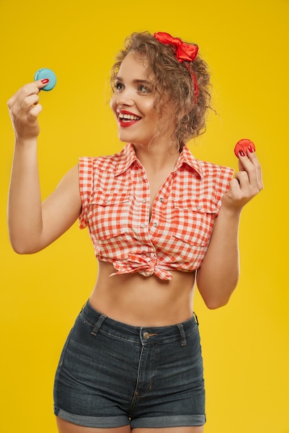 Mulher loira feliz mantendo dois biscoitos coloridos no estúdio