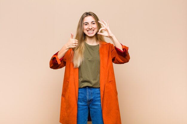 Mulher loira feliz, maravilhada, satisfeita e surpresa, mostrando gestos de ok e polegar para cima, sorrindo