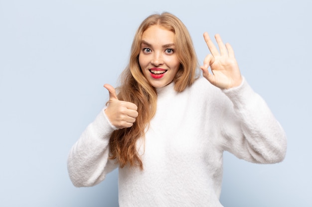 Mulher loira feliz, maravilhada, satisfeita e surpresa, mostrando gestos de ok e polegar para cima, sorrindo