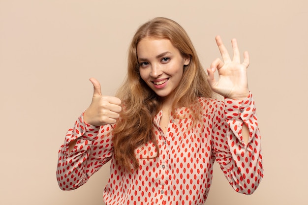 Mulher loira feliz, maravilhada, satisfeita e surpresa, mostrando gestos de ok e polegar para cima, sorrindo