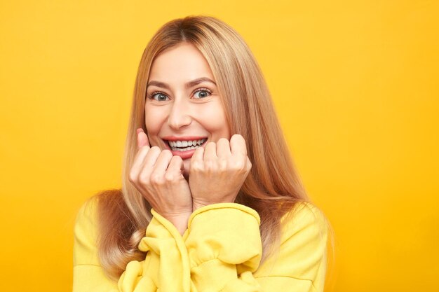 Mulher loira feliz sorrindo comemorando a vitória se alegra cerrando os punhos isolados em fundo amarelo