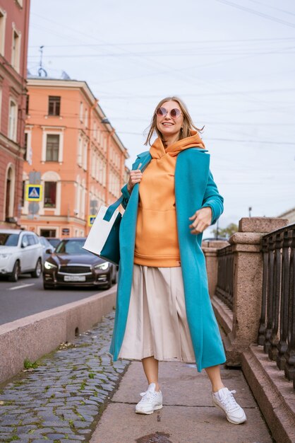 Mulher loira fofa feliz posando nas ruas da cidade com casaco azul