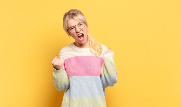 Mulher loira gritando agressivamente com uma expressão de raiva ou com os punhos cerrados celebrando o sucesso