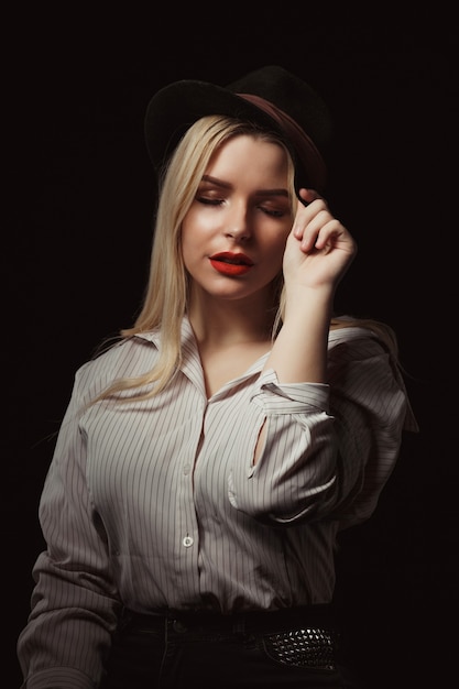 Mulher loira incrível de óculos e chapéu, posando com uma luz dramática no estúdio