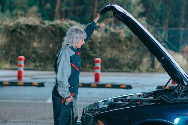 Mulher loira jovem atraente vestindo um uniforme de mecânico de automóveis e reparar o carro