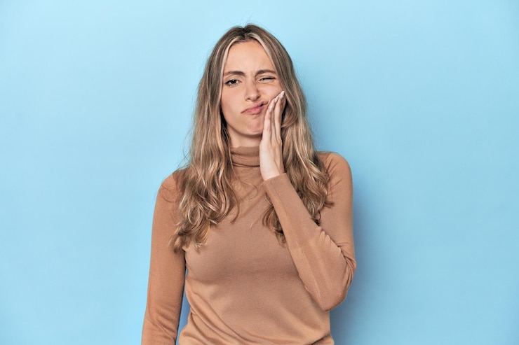Foto mulher loira jovem caucasiana em estúdio azul tendo uma forte dor de dentes dor molar