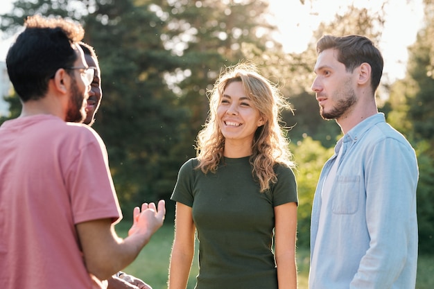 Mulher loira jovem e feliz com um sorriso largo, olhando para um dos três rapazes interculturais enquanto discute notícias curiosas com eles