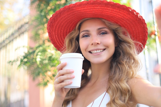 Mulher loira jovem feliz sorrindo amplamente, fazendo auto-retrato no seu dispositivo ao ar livre.