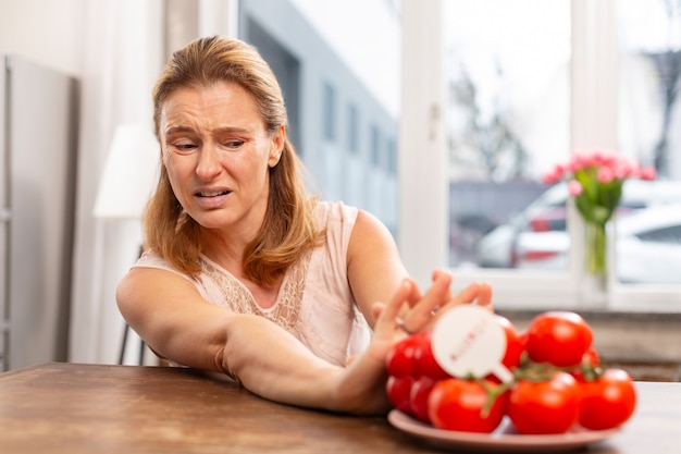 Mulher loira madura de olhos escuros que não come tomates enquanto se sente alérgica