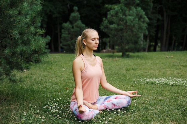 Mulher loira meditando na grama verde